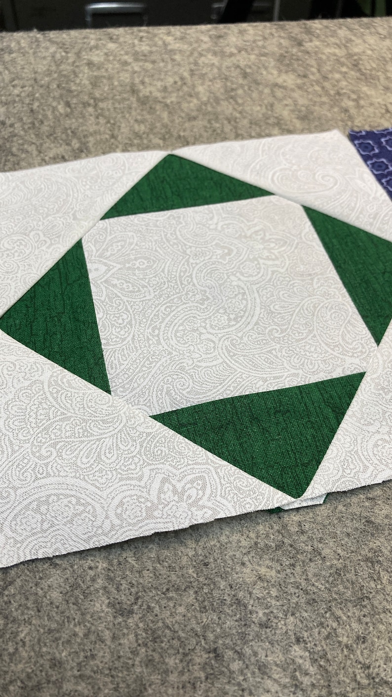 May include: A white fabric with a paisley pattern is cut into a square shape. Four green fabric triangles are sewn onto the white fabric, forming a diamond shape in the center.
