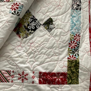 May include: A white quilt with a red and green holly leaf pattern. The quilt is made of various fabrics with different patterns, including snowflakes, candy canes, and geometric designs.