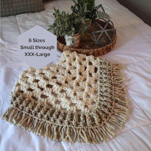 May include: A cream-colored crocheted poncho featuring a granny square pattern and a fringed hem with brown speckled accents. A light purple hexagon overlay displays the text 6 Sizes Small through XXX-Large in black lettering.