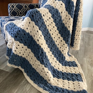 Puede incluir: Una manta de punto de crochet con rayas azules y blancas. La manta está hecha con un hilo grueso y tiene un diseño simple y moderno.