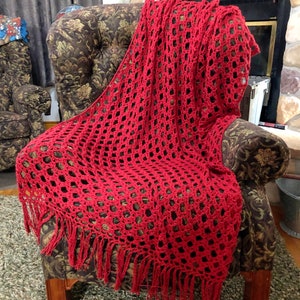 Può includere: Una coperta di uncinetto rossa con frange su una poltrona con motivo marrone.