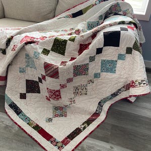 May include: A white quilt with a red, green, and blue patchwork design. The quilt is folded and draped over a white couch.
