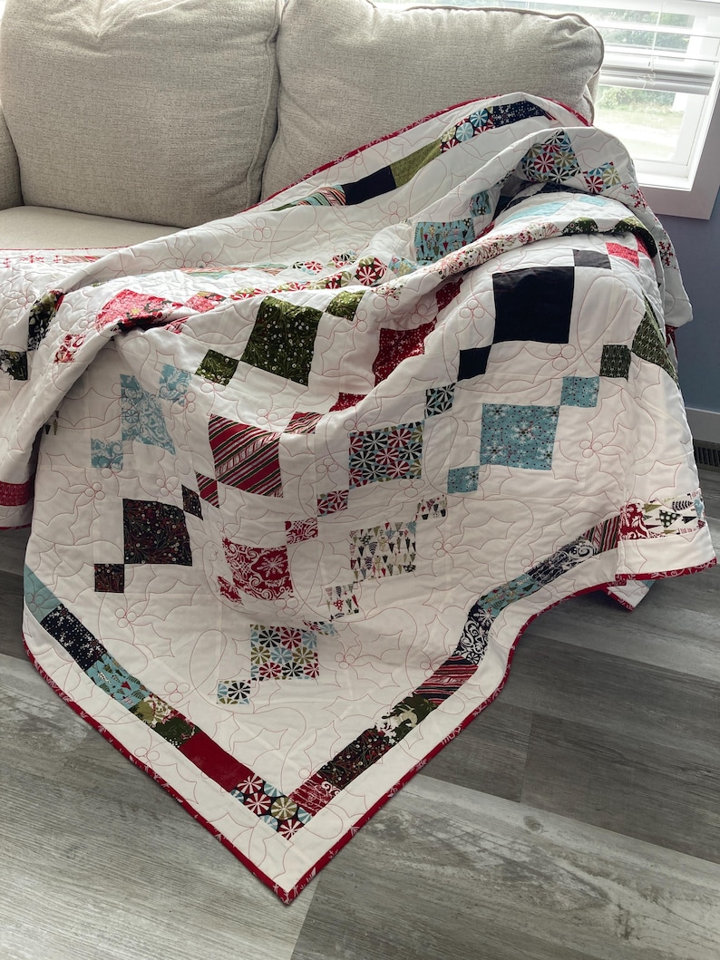 May include: A white quilt with a red, green, and blue patchwork design. The quilt is folded and draped over a white couch.