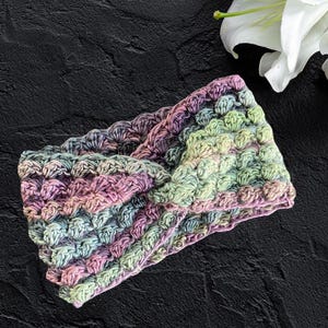 May include: A multi-colored crocheted headband with a twisted design. The headband is made with a variety of shades of pink, green, and blue yarn.