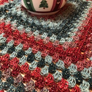 Könnte beinhalten: Nahaufnahme eines gehäkelten Tischläufers in Rot, Blau und Grün. Der Läufer hat einen glitzernden goldenen Faden, der durchgewebt ist.