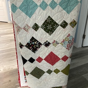 May include: A white quilt with a diamond pattern in various colors, including red, green, blue, and black. The quilt is quilted with a holly leaf design.