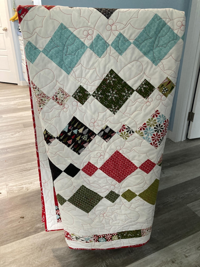 May include: A white quilt with a diamond pattern in various colors, including red, green, blue, and black. The quilt is quilted with a holly leaf design.