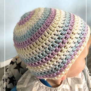 May include: A baby wearing a crocheted hat with stripes of light blue, cream, and purple. The hat is made with a simple stitch and has a loose fit. The baby is wearing a gray bib with a chevron pattern.