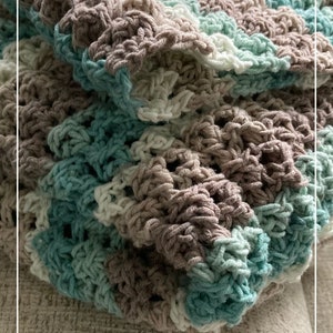 May include: A crocheted blanket in shades of teal, brown, and white. The blanket is folded and draped over a light brown couch. The text "Patternprincess.com" is visible in the bottom right corner of the image.
