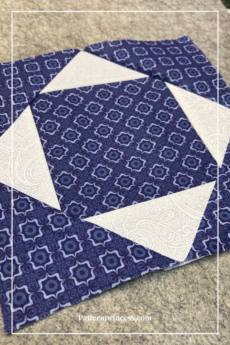 May include: A blue and white quilt block with a geometric pattern. The block is made up of four triangles and a square in the center. The triangles are white with a paisley pattern and the square is blue with a geometric pattern.