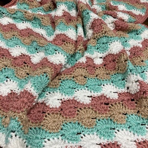 May include: A crocheted blanket with a striped pattern in shades of pink, white, beige, and teal.