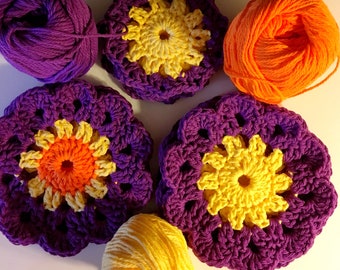 May include: Five crocheted flower motifs in shades of purple, yellow, and orange. The motifs are arranged in a circle with a ball of yellow yarn in the center.