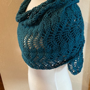 May include: Teal crochet shawl with a delicate openwork pattern. The shawl is draped over a white dress form.