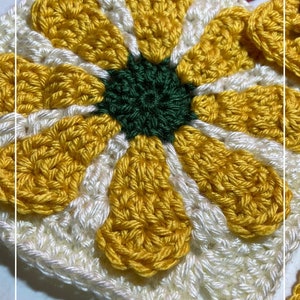 Puede incluir: Un cuadrado de crochet con forma de flor con un centro amarillo y pétalos blancos. El centro de la flor es verde. El cuadrado está hecho con hilo blanco y tiene un borde amarillo.