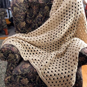 May include: A beige crocheted throw blanket with a lacy pattern draped over a floral patterned armchair.