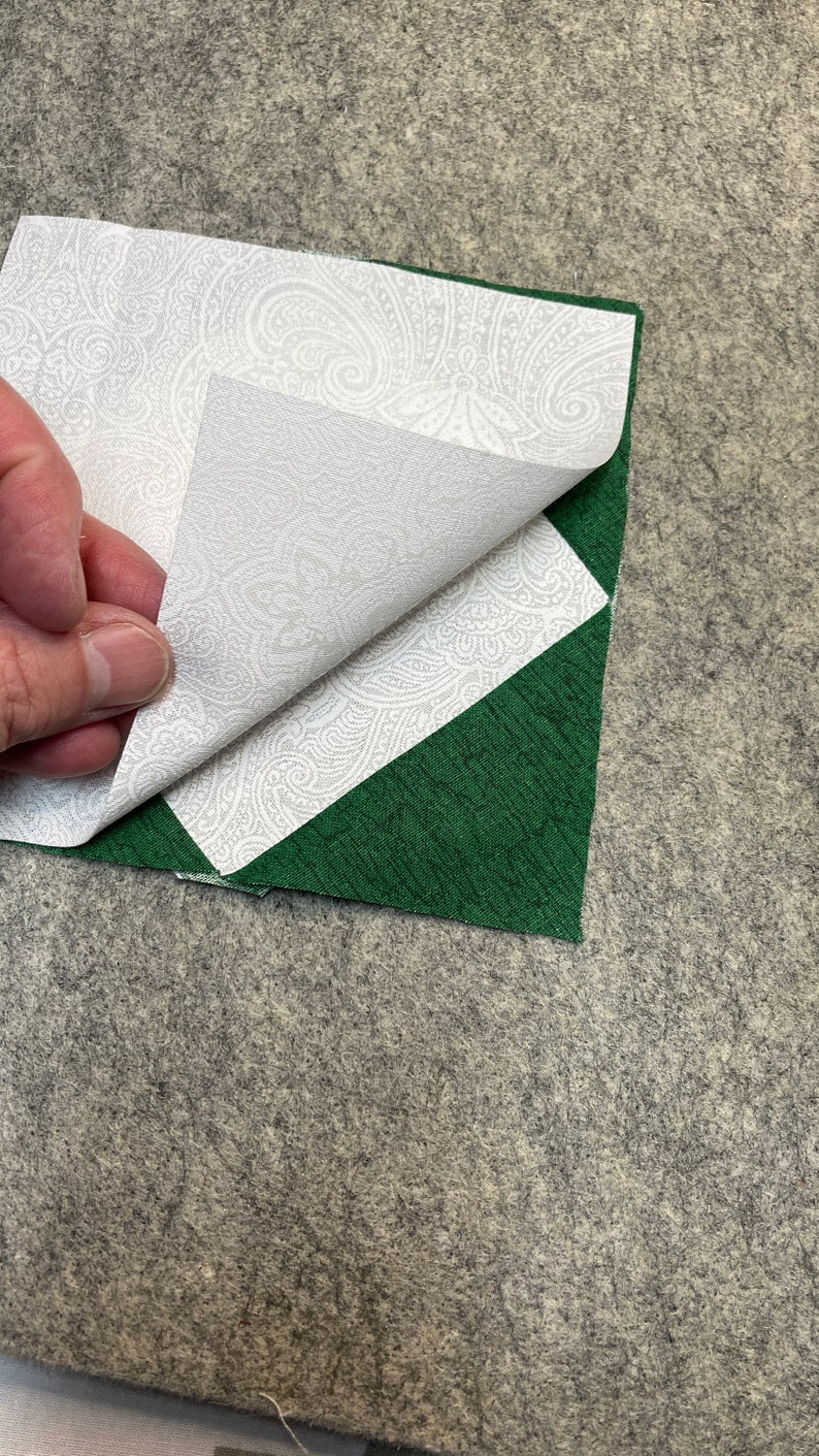 May include: A white fabric with a paisley pattern is folded over a green fabric square. The fabrics are on a gray surface.