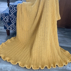 Könnte beinhalten: Eine gelbe Häkeldecke mit einem gewellten Rand. Die Decke liegt über einem Stuhl.