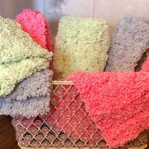 May include: A set of five fluffy, knitted dishcloths in a wire basket. The dishcloths are in shades of light green, pink, and lavender.