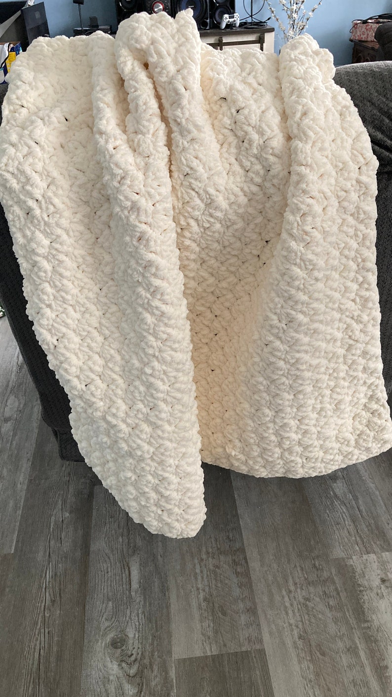 May include: A white crocheted blanket with a textured pattern. The blanket is folded and draped over a chair. Beginner Super Bulky Crochet Blanket Pattern Printable PDF, beginner friendly, Easy Crochet Chunky Blanket, Simple Crochet Pattern Modern