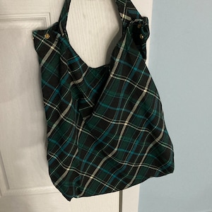 May include: A green and black plaid tote bag with a white handle. The bag is hanging on a white door.