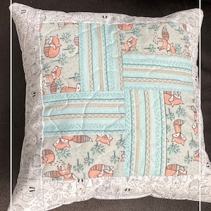 Könnte beinhalten: Ein hellblaues und weiß gemustertes Kissen mit einem Fuchs-Design. Das Kissen ist gesteppt und hat einen weißen Rand. Das Kissen liegt auf einem braunen Sofa.