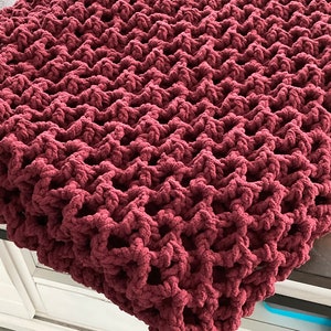 Puede incluir: Una manta de punto de ganchillo de color burdeos con una textura de punto grueso.