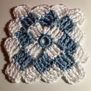 Puede incluir: Un cuadrado tejido a crochet con un patrón geométrico blanco y azul. El cuadrado está hecho con punto bajo y tiene una textura en relieve.