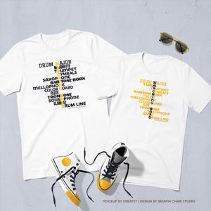 May include: Two white short-sleeve t-shirts featuring a black and yellow graphic print of marching band instruments and roles arranged in a cross pattern. The design includes the text MARCHING BAND. Also includes a pair of white sneakers with yellow accents and black laces, and a pair of black-framed sunglasses.
