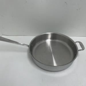 May include: Stainless steel frying pan with a long handle and a smaller loop handle on the opposite side. The pan has a wide, shallow cooking surface and is made of a shiny, silver-colored metal. This cookware is suitable for various cooking tasks.