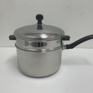 May include: Stainless steel steamer pot with a black handle and lid knob. The pot has a two-tiered design, with a lid and a steamer basket. The handle has a loop for hanging. The pot is designed for cooking vegetables and other foods.