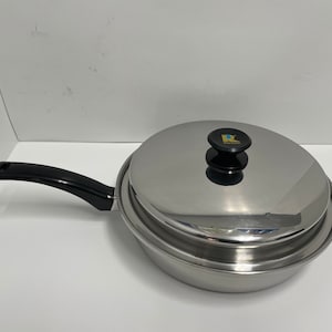 May include: A silver stainless steel frying pan with a black handle and a matching lid. The lid has a black knob with a gold logo that says "R" with a blue drop of water.