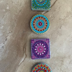 May include: Four decorative compact mirrors with colorful jeweled mandala designs. The mirrors are square and round in shape.