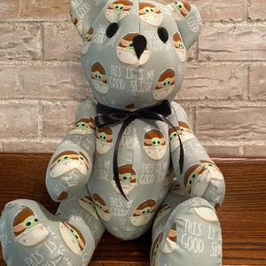 K&ouml;nnte beinhalten: Ein grauer Pl&uuml;schteddyb&auml;r mit einer schwarzen Schleife. Der B&auml;r ist mit einem Muster eines gr&uuml;nen Alien-Charakters bedeckt, auf dem der Text "This is my good side" wiederholt auf dem Stoff steht.