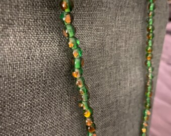 May include: A green and gold glass bead necklace. The beads are faceted and have a shimmery finish.