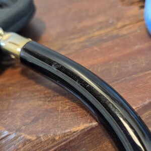 Pode incluir: Close-up de uma ma&ccedil;aneta preta e dourada, possivelmente para uma porta ou gaveta. A ma&ccedil;aneta &eacute; curva e tem um acabamento brilhante. A parte dourada parece ser um detalhe decorativo.