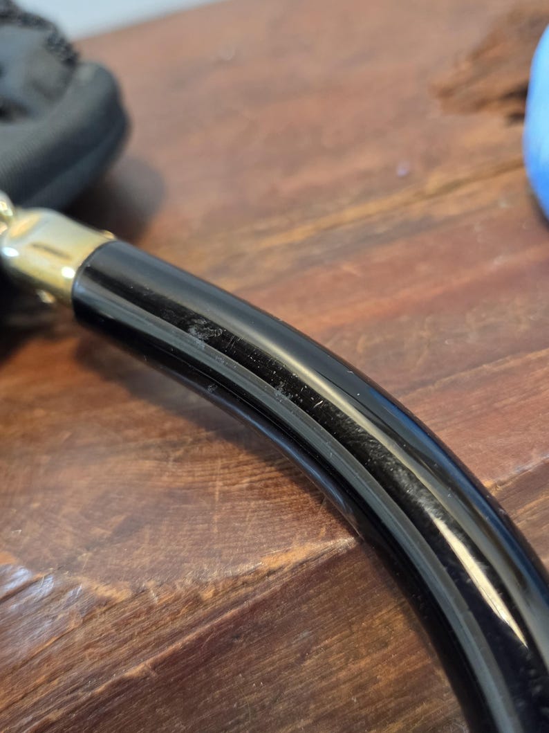 Pode incluir: Close-up de uma ma&ccedil;aneta preta e dourada, possivelmente para uma porta ou gaveta. A ma&ccedil;aneta &eacute; curva e tem um acabamento brilhante. A parte dourada parece ser um detalhe decorativo.
