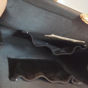 Pode incluir: Bolsa de noite de cetim preto com fecho dourado. O interior apresenta um bolso de veludo preto e uma pequena etiqueta. A bolsa est&aacute; aberta, revelando o forro e os compartimentos.
