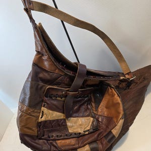 May include: A brown leather shoulder bag with a patchwork design. The bag features various shades of brown leather pieces stitched together, a long shoulder strap, and a smaller pocket on the front. The bag is a hobo style.