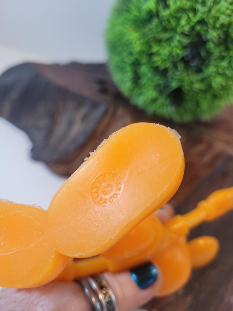 May include: Orange plastic toy figure with a circular logo on the bottom that reads "Made in Hong Kong".