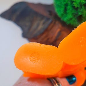 May include: Orange rubber toy shaped like a cartoon character. The toy has a round bottom with a circular imprint that reads "Made in China".