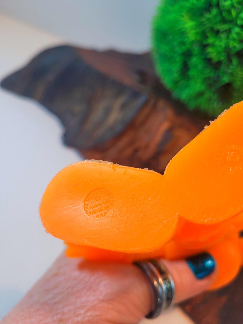 May include: Orange rubber toy shaped like a cartoon character. The toy has a round bottom with a circular imprint that reads "Made in China".