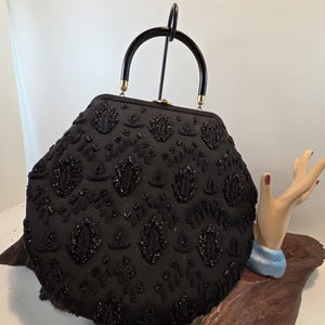 Pode incluir: Uma bolsa preta com contas, com formato arredondado e al&ccedil;a preta. A bolsa &eacute; coberta por intrincados trabalhos de contas, com padr&otilde;es florais e de folhas. A al&ccedil;a tem um design curvo.