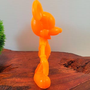 May include: Orange plastic figurine of a cartoon mouse. The mouse is standing with its arms at its sides and its head tilted to the side. The figurine is about 6 inches tall.