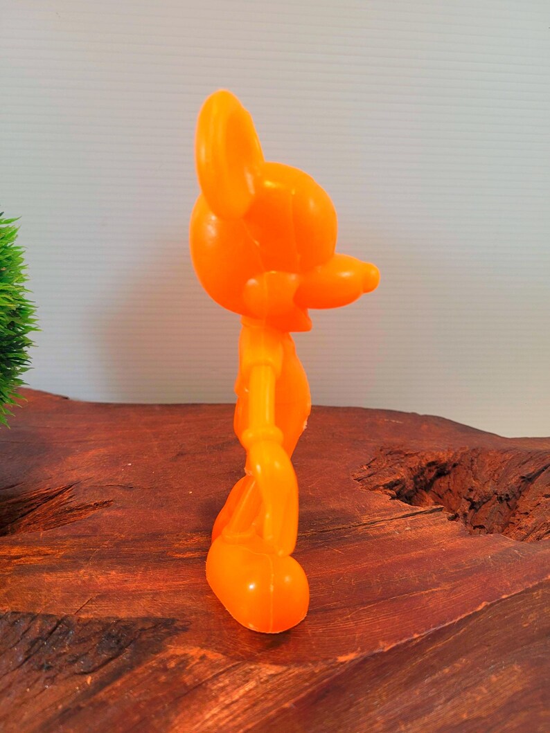 May include: Orange plastic figurine of a cartoon mouse. The mouse is standing with its arms at its sides and its head tilted to the side. The figurine is about 6 inches tall.