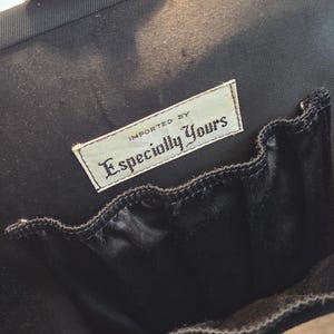 Pode incluir: Interior de uma mala preta com um pequeno bolso e uma etiqueta que diz "Imported By Especially Yours". A mala tem um fecho dourado.