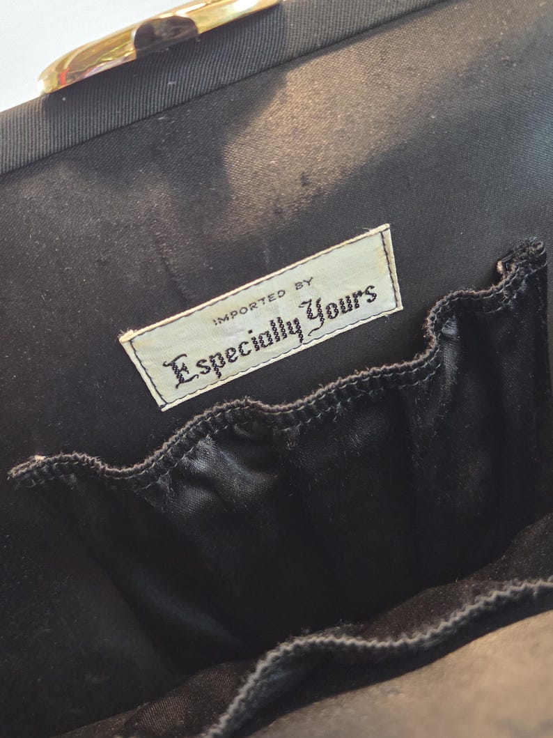 Pode incluir: Interior de uma mala preta com um pequeno bolso e uma etiqueta que diz "Imported By Especially Yours". A mala tem um fecho dourado.