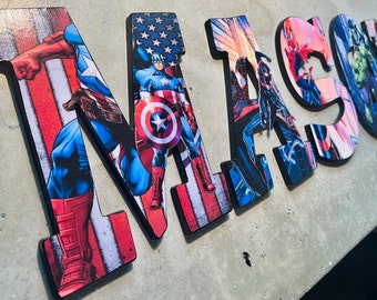 May include: Wooden letters spelling out the name "MASON" with a superhero theme. Each letter is decorated with a different superhero image, including Captain America, Spiderman, and the Hulk.