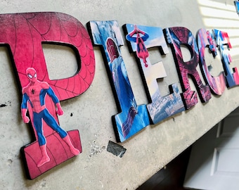 May include: A set of large, three-dimensional wooden letters spelling the name PIERCE, decorated with vibrant Spider-Man graphics. Each letter features a unique scene or character pose from the Spider-Man universe in red, blue, and black.