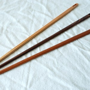 May include: Three wooden knitting needles with a hole at the end. The needles are different colors: natural wood, dark brown, and reddish brown.