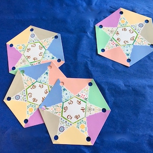 May include: Three hexagonal paper cards featuring a central white star shape with floral patterns in pastel shades of yellow, purple, blue, and pink. Each card has circular holes at the corners and displays the text A1, B2, C3, D4, E5, and F6.